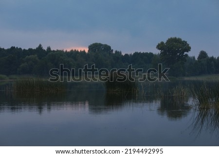 Early morning on the river.View of the blue sky the water and the shore in the fog through the tall grass at dawn