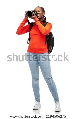 people, profession and photography concept - happy smiling woman photographer with digital camera and backpack photographing over white background