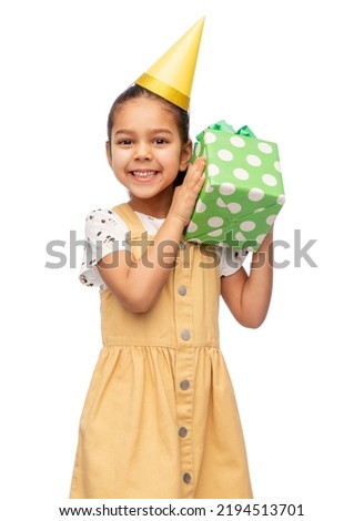 birthday, childhood and people concept - portrait of smiling little girl in dress and party hat with gift box over white background