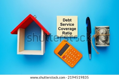 A picture house miniature, with fake money, Debt Service Coverage Ratio on notepad, calculator, and pen on blue background. Royalty-Free Stock Photo #2194519835