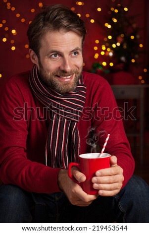 Christmas - happy smiling forty years old caucasian man holding hot drink or cocoa on dark red background with lights.