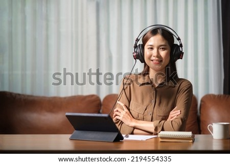 Beautiful young woman in headphones sitting front of microphone and laptop in her studio.