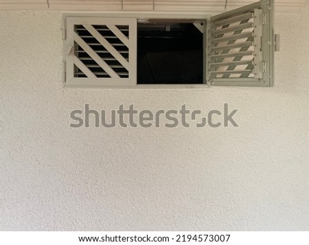 half opened window with ventilation grilles in a white wall