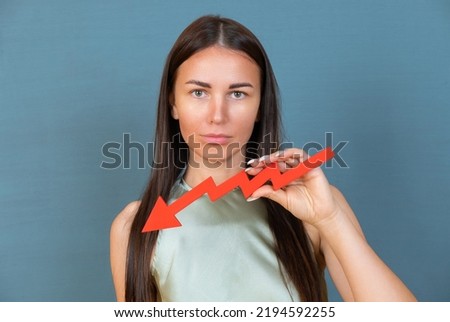 Sad businesswoman holds a red arrow chart pointing down. The concept of reducing costs and profits, falling living standards and prices. Decreased projections, depressed economies.