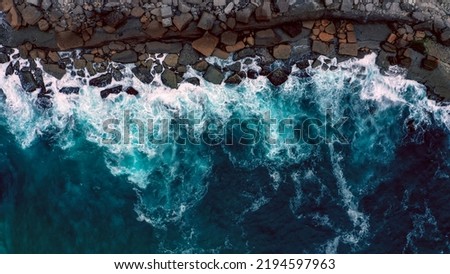 Drone view over  sea water surface the rocky shore. Top view over rolling ocean waves to the rocky shore.  Aerial view of the beautiful ocean and rocky shore with rolling waves on the summer day. Royalty-Free Stock Photo #2194597963