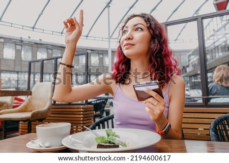 the girl raised her hand and calls the waiter to pay for breakfast in the cafe with a card