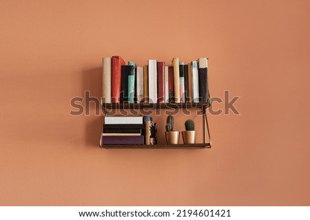 Books stack on hanging shelf. Coral peach wall background. Aesthetic minimal interior design. Reading, education concept with bookshelf Royalty-Free Stock Photo #2194601421