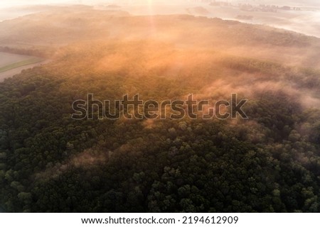 Orange sunrise glare on thick fog covering green forest and field in Roztocze Poland. Top-down view. Horizontal shot. High quality photo