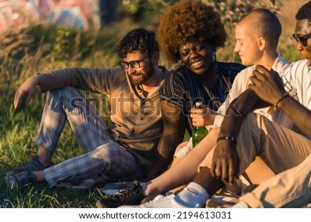 near while sitting on the grass, drinking beer, talking and laughing. Summer holidays. High quality photo