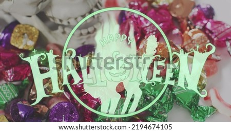 Happy halloween text banner with pumpkin icon against close up of halloween candies on white surface. halloween festivity and celebration concept