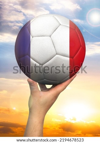 Soccer ball in hand with a depiction of the flag of France against a colorful sky Royalty-Free Stock Photo #2194678523