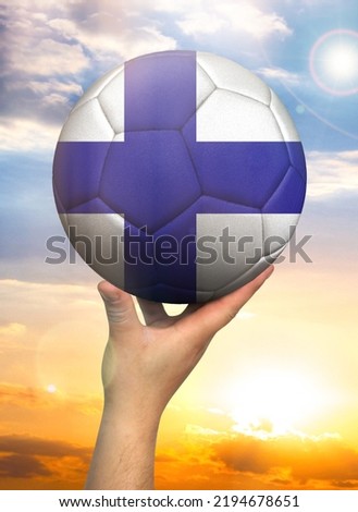 Soccer ball in hand with a depiction of the flag of Finland against a colorful sky
