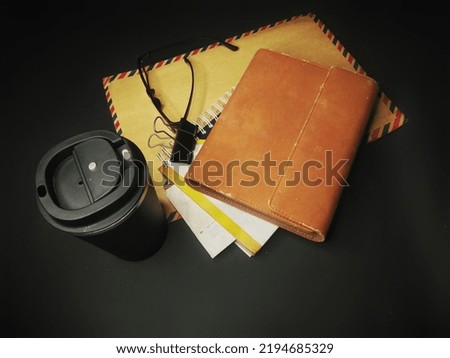 brown book composition, brown envelope, coffee drinking bottle on black background