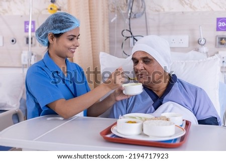 Young nurse feeding the senior patient lying on bed at hospital Royalty-Free Stock Photo #2194717923