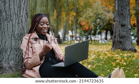 Excited african american woman sitting in autumn park playing online game on laptop gambling competition happy young girl winner celebrating victory enjoying success winning lottery using computer Royalty-Free Stock Photo #2194723635