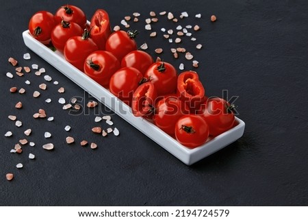 An elongated plate of tomatoes, paprika and coarse pink Tibetan salt on a black concrete table. High angle with copy space Royalty-Free Stock Photo #2194724579
