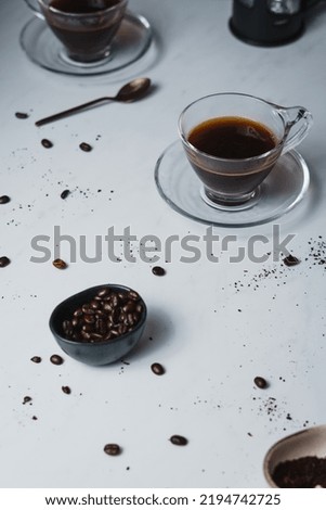 Contemporary style coffee food and drink photo. Set against a white background. Black coffee in glass cup and saucer.