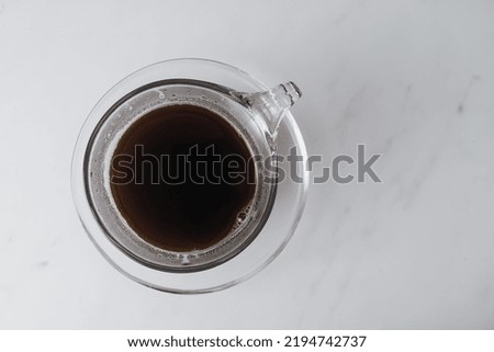 Contemporary style coffee food and drink photo. Set against a white background. Black coffee in glass cup and saucer.