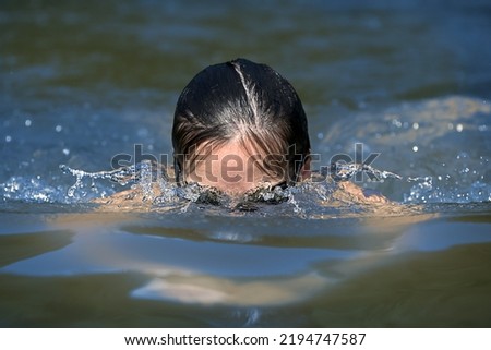 Breaststroke swimming. Female swimmer with black glasses partially under water approaching fast in natural water. Fast shutter. 
