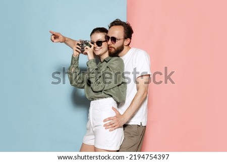 Taking picture. Happy couple in love, handsome man and charming girl posing isolated over blue-pink background. Fashion, emotions, youth, love, travel, vacation concept