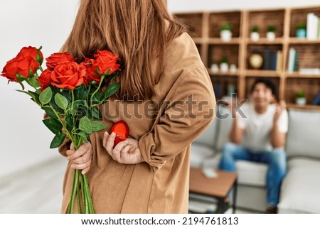 Woman suprising man with bouquet of roses at home.