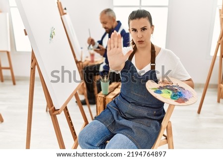 Young artist woman at art studio with open hand doing stop sign with serious and confident expression, defense gesture 