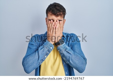 Young hispanic man standing over blue background rubbing eyes for fatigue and headache, sleepy and tired expression. vision problem 