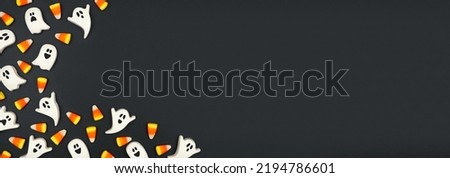 Halloween corner border of candy corn and spooky chocolate ghosts. Overhead view on a black banner background. Copy space. Royalty-Free Stock Photo #2194786601