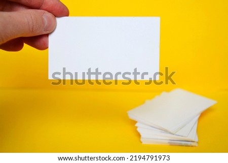 Holding blank white business card with a stack of business cards and simple yellow background