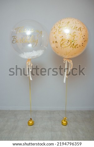 Two large balloons with confetti and feathers, helium balloons on the background of the wall