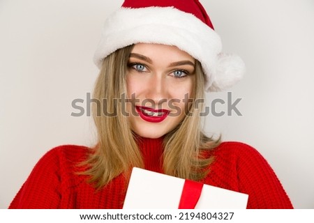 Closeup portrait of female blond in red sweater with santa hat smiling and holding present. Chistmas eve,holidays concept