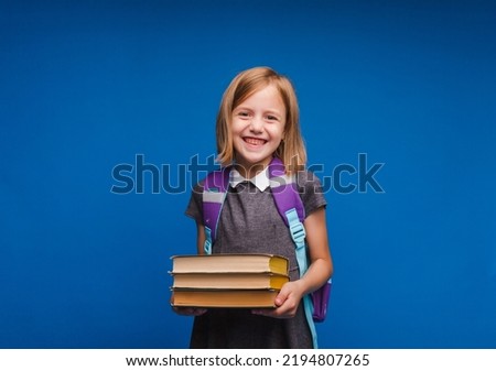 a happy teenage girl in a school uniform holds a stack of books. Banner of a schoolgirl. Portrait of a schoolgirl with space to copy on a blue background.