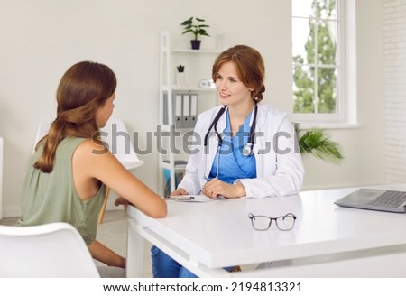 Doctor pediatrician talking to teenage girl patient telling her about medical care in hospital. Friendly female doctor fills out form sitting at table with girl in medical office. Concept of