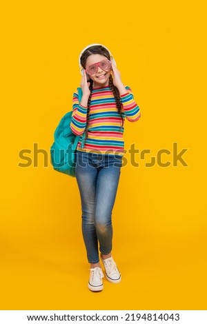 Happy teenage girl listening to music after school yellow background, school. Music school