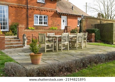 Garden patio in winter in an English garden. Paved terrace with teak furniture outside an old character house, UK