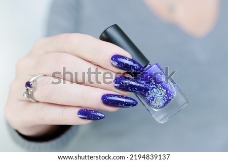 Woman's beautiful hand with long nails and blue purple manicure with bottles of nail polish