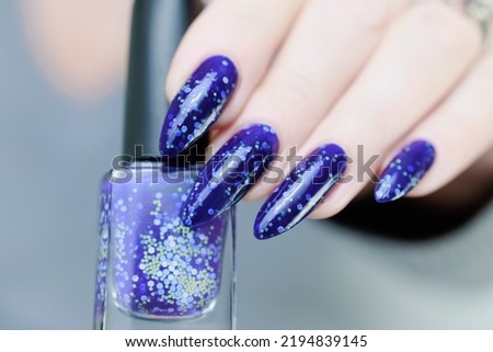 Woman's beautiful hand with long nails and blue purple manicure with bottles of nail polish