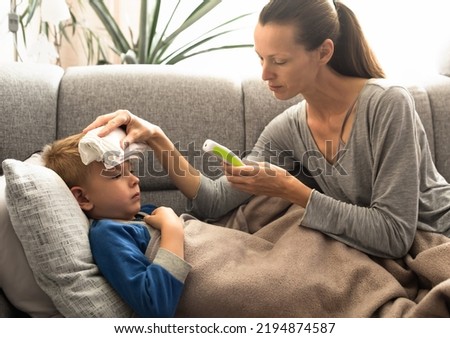 Mother taking her sick child's temperature. Mom taking care of child at home with fever.  Royalty-Free Stock Photo #2194874587