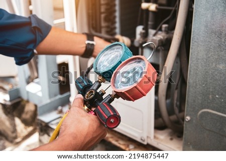 Heat and Air Conditioning, HVAC system service technician using measuring manifold gauge checking refrigerant and filling industrial air conditioner after duct cleaning maintenance outdoor compressor. Royalty-Free Stock Photo #2194875447
