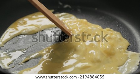 making scrambled eggs on nonstick pan, mixing with wooden spatula, wide photo Royalty-Free Stock Photo #2194884055