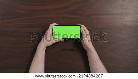 Top view man hand hold smartphone with green screen over black walnut wood table, wide photo