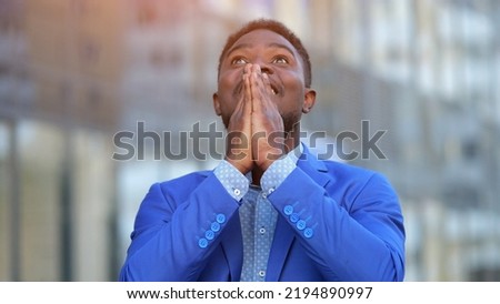 African American man thanks God for having business and being successful. Mature entrepreneur looks with happy expression against blurry building, sunlight Royalty-Free Stock Photo #2194890997