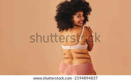 Curvy young woman embracing herself and smiling at the camera while wearing underwear. Body positive woman with an Afro hairstyle feeling comfortable in her natural body and curly hair.