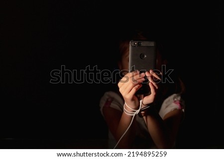 Mobile addiction and digital dependence concept. Young girl tied with cell phone charger cord and holds smartphone. Copy space for design. Horizontal image. Royalty-Free Stock Photo #2194895259