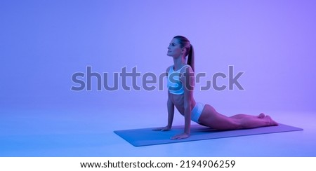 Fitness woman making cobra pose on yoga mat in blue gradient neon light with copy space background for your advertising content on the right. Keep fit. Healthy lifestyle