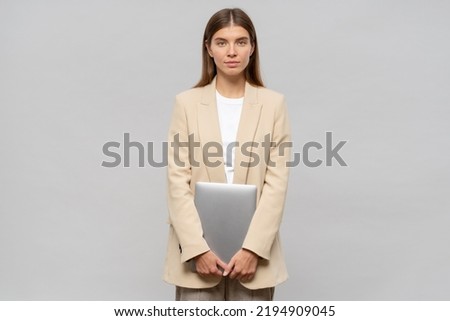 Shy female student feeling nervous waiting for results of exam standing on gray background with laptop in hands. Education and technology Royalty-Free Stock Photo #2194909045