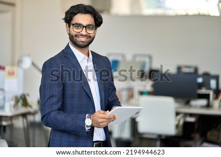 Smiling young indian business man professional project manager, arab company employee, eastern businessman executive financial banker wearing suit standing in office holding digital tablet, portrait Royalty-Free Stock Photo #2194944623