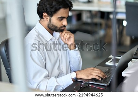 Busy young indian business man employee working using laptop, analyzing financial market, developing online project data, thinking on plan looking at computer, doing accounting management in office. Royalty-Free Stock Photo #2194944625
