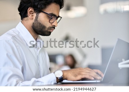 Busy young indian or arab professional business man software engineer, male manager worker using laptop computer working in office analyzing data technology typing sitting at workplace.