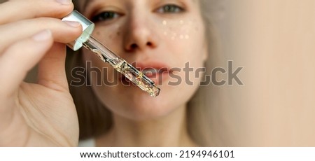 A woman shows a dropper with a serum with gold particles to the camera. Selective focus.